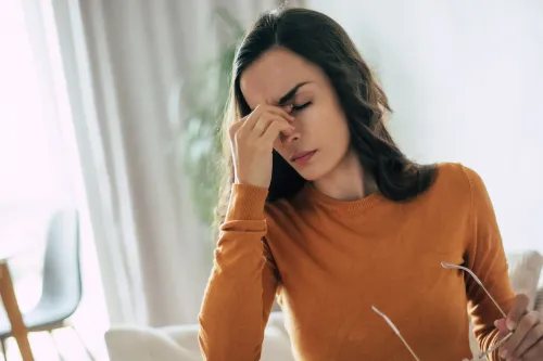 A woman holding her forehead in visible stress, symbolizing the impact of stress on menstrual health.