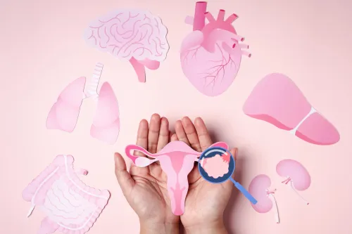 Hands gently holding a paper-cut uterus surrounded by pink illustrations of major organs, with a magnifying glass highlighting the ovaries—symbolizing the complexity of PCOS and its impact on the whole body.